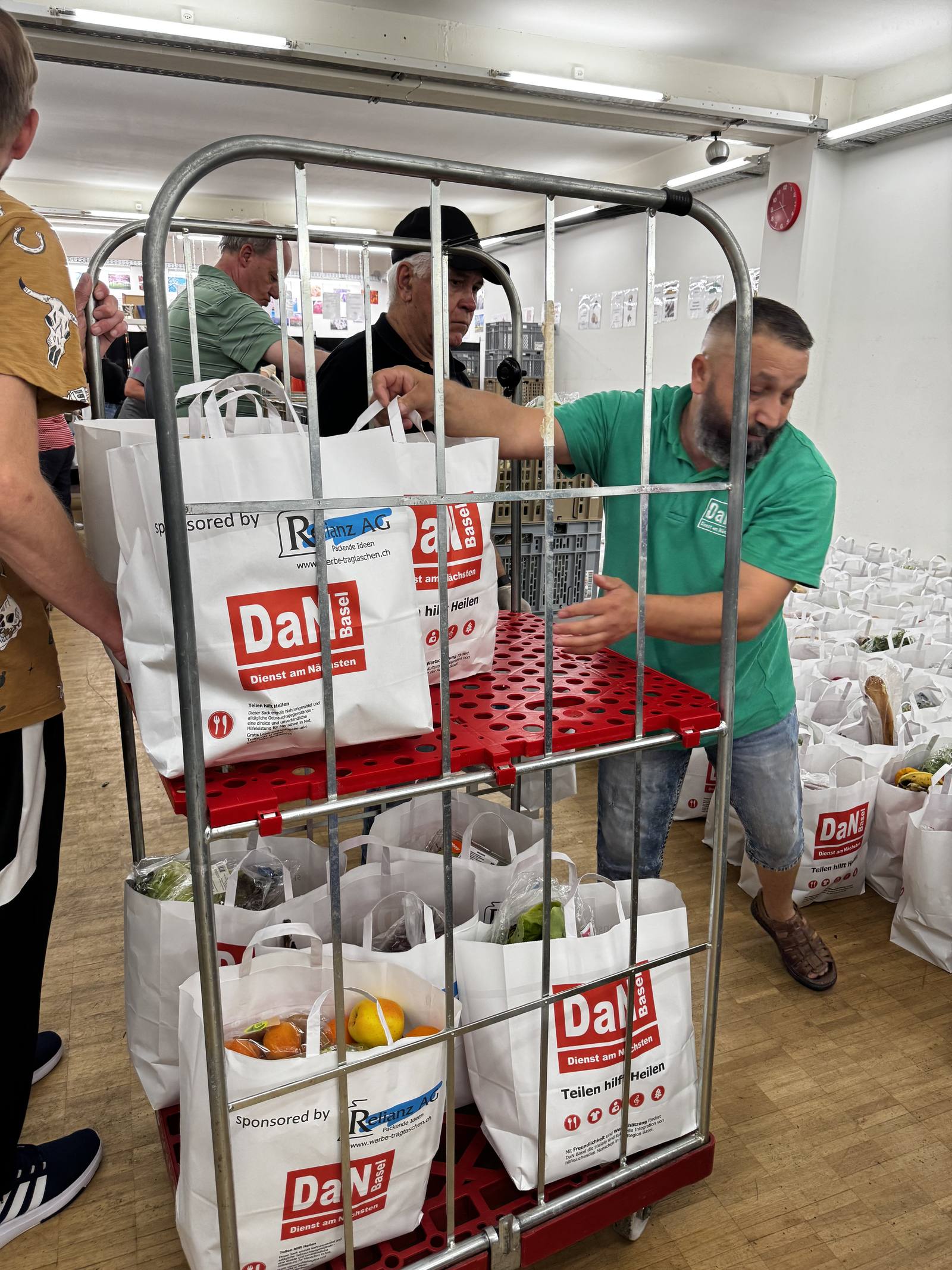 Ein Helfer transportiert einen Rollwagen voller Taschen zur Ausgabe.